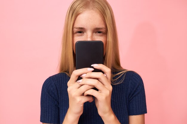 金髪の若い女性が目を細め、携帯を持って不審な表情をしている
