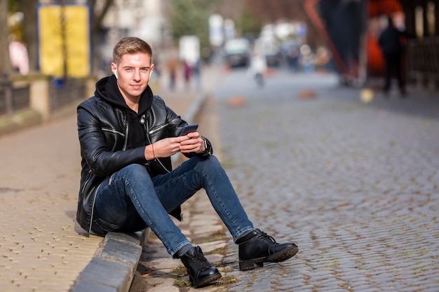 Blonde young man listening to music on earbuds outside