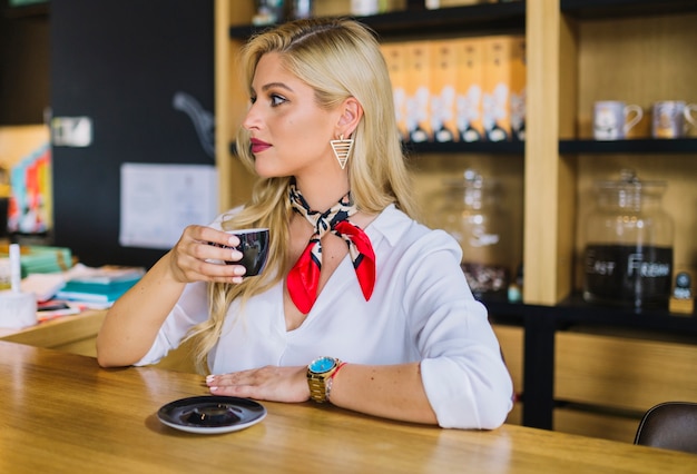 Foto gratuita giovane donna bionda che tiene tazza di caffè nera nel cafã