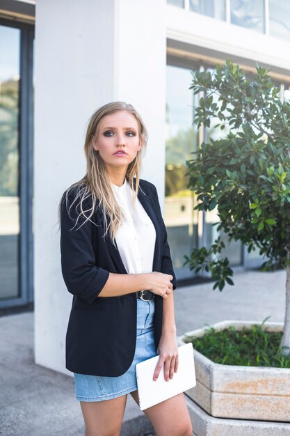 Blonde young woman holding digital tablet standing at outdoors