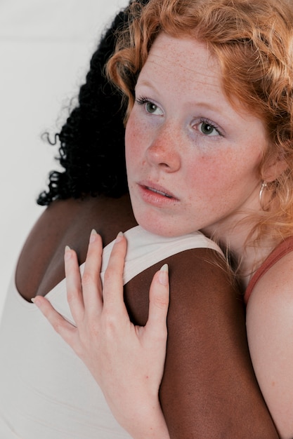 Free photo blonde young woman hugging her african friend with dark skinned