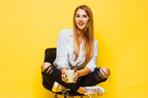 뜨거운 커피 한 잔을 들고 비즈니스 의류를 입고 고립 된 노란색 벽 위에 금발의 젊은 여자.
