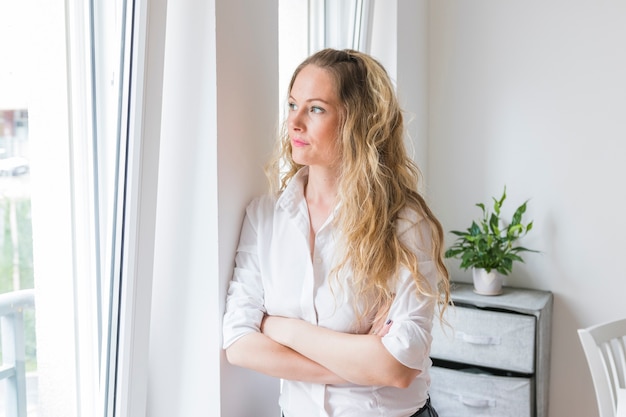 Giovane donna bionda che si appoggia sulla parete guardando la finestra