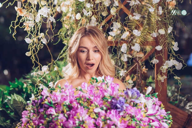 Blonde young woman looking at large flower bouquet surprisingly