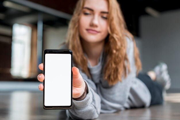 Блондинка молодая женщина, лежа на полу, показывая мобильный телефон с белым экраном