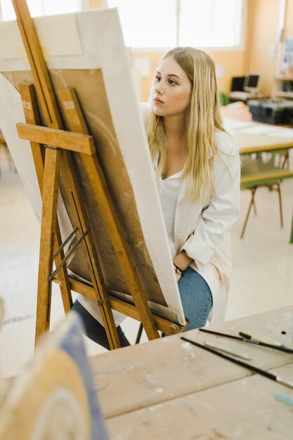 Blonde young woman painting on easel