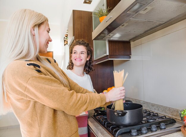 Blonde young woman preparing spaghetti with her female friend