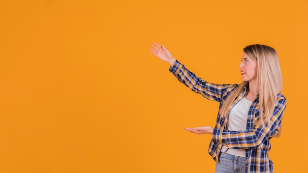 Blonde young woman presenting something against an orange background