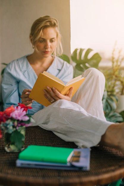 Blonde young woman reading book with vase on table