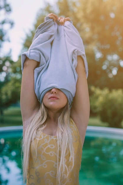 Free photo blonde young woman removing t-shirt over head at outdoors