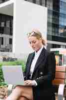 Free photo blonde young woman sitting on bench using laptop