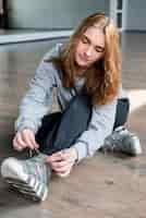 Free photo blonde young woman sitting on hardwood floor tying shoelace