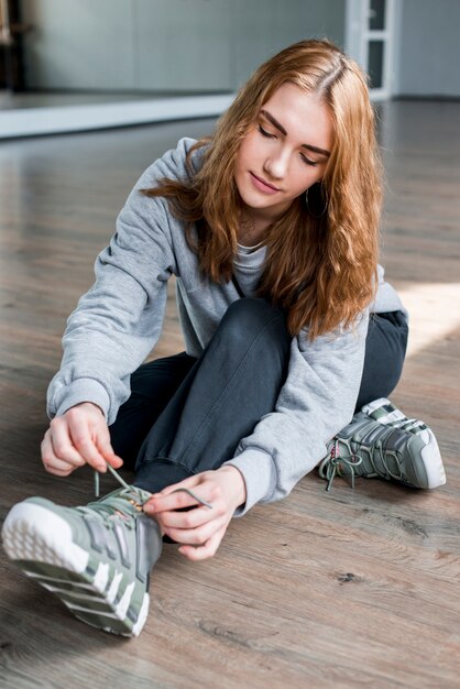 Blonde young woman sitting on hardwood floor tying shoelace