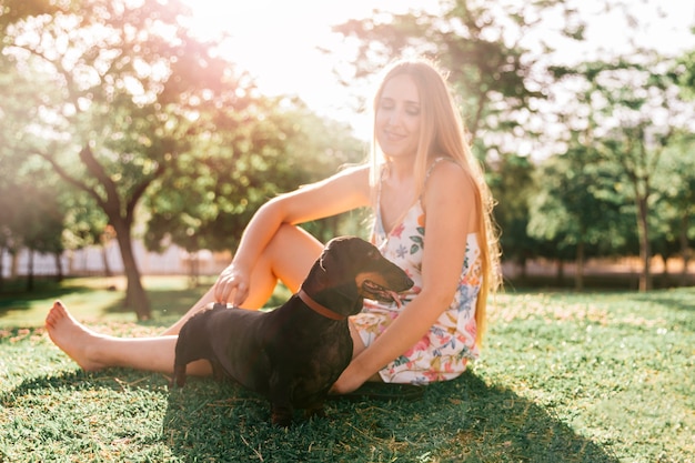 무료 사진 금발의 젊은여자가 공원에서 그녀의 강아지와 함께 앉아