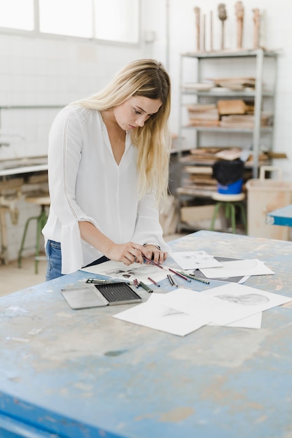 Blonde young woman sketching on white paper in workshop