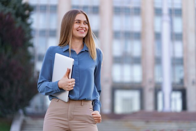 Blonde young woman smiling portrait wearing blue gentle shirt over building