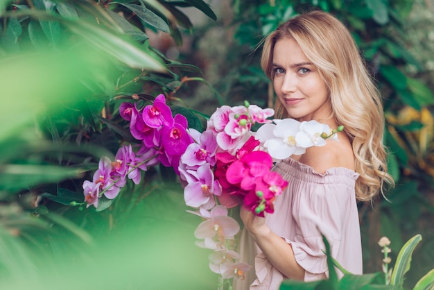 Blonde young woman standing in garden holding orchid