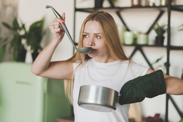 Blonde young woman tasting soup from the ladle