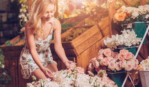 Blonde young woman touching the roses in the florist shop