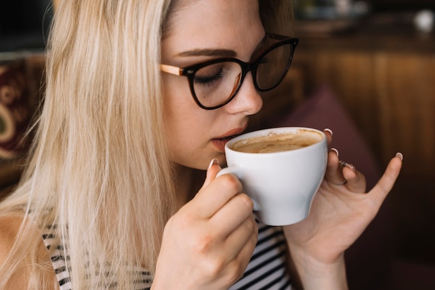 커피를 마시는 안경을 쓰고 금발의 젊은 여자