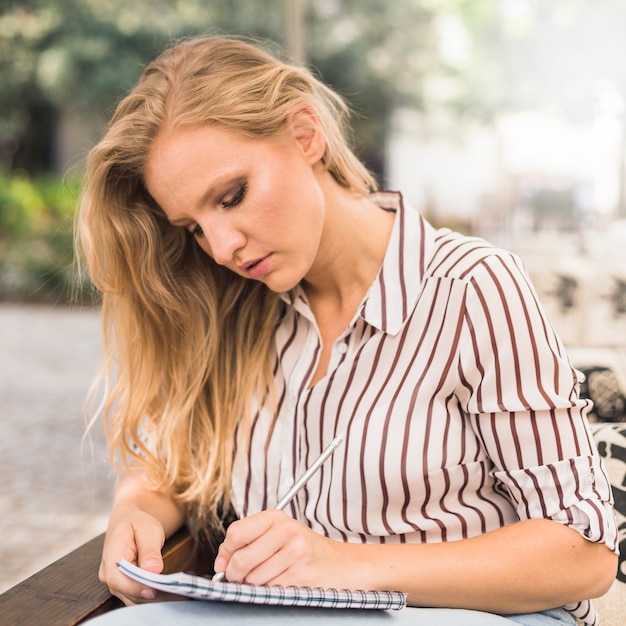 Blonde young writing on notebook with pencil