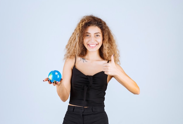 Блонди девушка держит мини-глобус и чувствует себя позитивно.