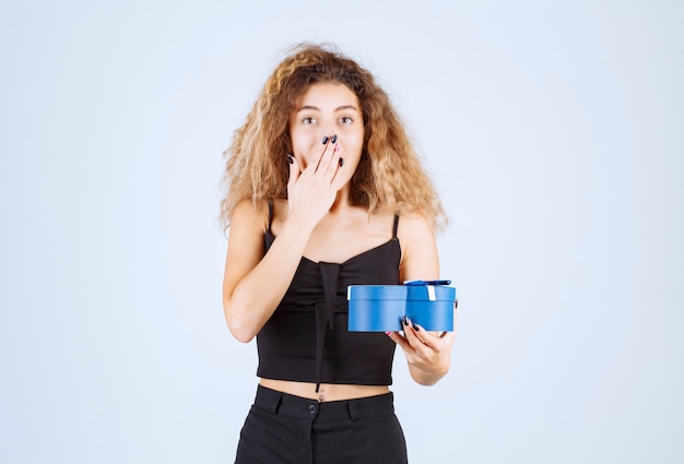 Blondie girl holding a blue gift box and looks surprized. 