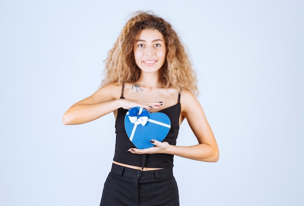 Free photo blondie girl holding a blue gift box and looks surprized.