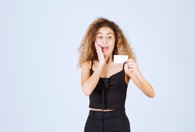 Blondie girl holding a business card and looks surprized. 