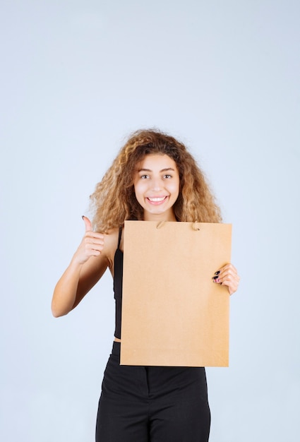 Foto gratuita ragazza bionda che tiene in mano una borsa della spesa di cartone e indica un altro posto.