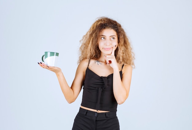 Ragazza bionda che tiene in mano una tazza di caffè e pensa.