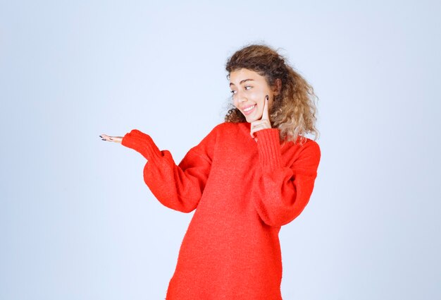 Blondie woman in red sweatshirt pointing somewhere on the left side.