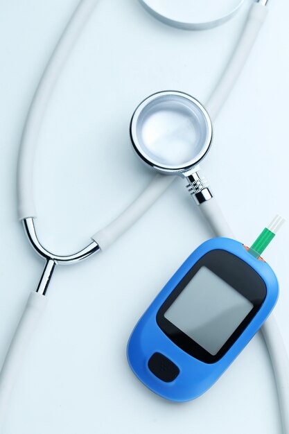 Blood glucose meter and stethoscope on white background
