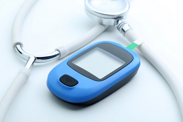 Blood glucose meter and stethoscope on white background