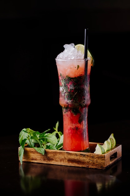 Bloody mary cocktail with red tomato sauce, herbs and ice cubes inside wooden tray.