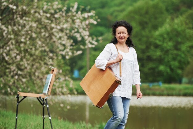 Blooming tree behind. Mature painter with case of instruments have a walk in the beautiful spring park