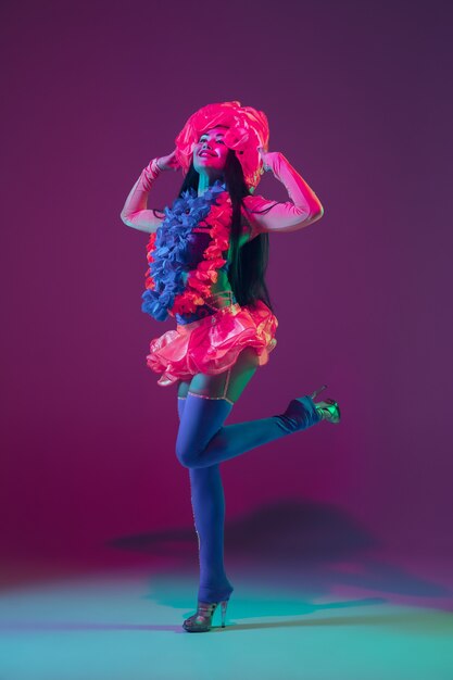 Blossom. Hawaiian brunette model on purple  wall in neon light. Beautiful women in traditional clothes smiling, dancing and having fun. Bright holiday's, celebration colors, festival.