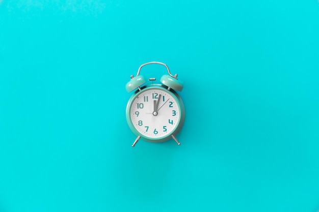 Blue alarm clock on blue background isolated flat lay