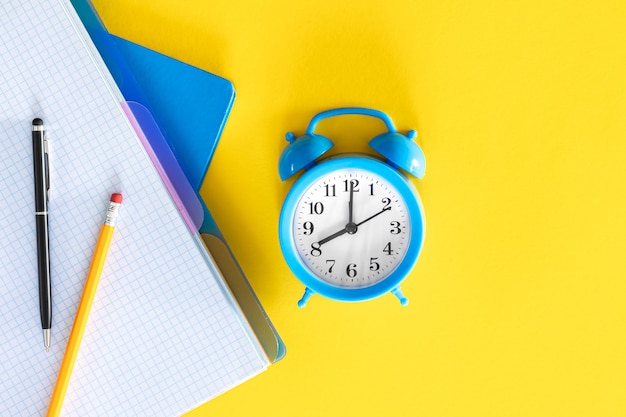 青い目覚まし時計と黄色い背景の平らなデザインのノートパッド