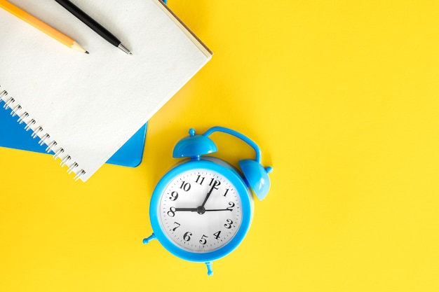 Free photo blue alarm clock and notepads on a yellow background flat design