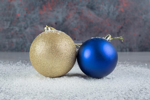 Синие и бежевые декоративные новогодние шары, сидящие в кокосовой пудре на мраморной поверхности