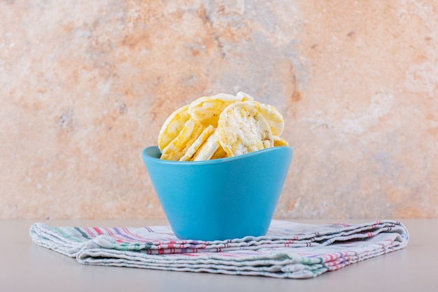 Blue bowl of crispy rice chips on white table. High quality photo