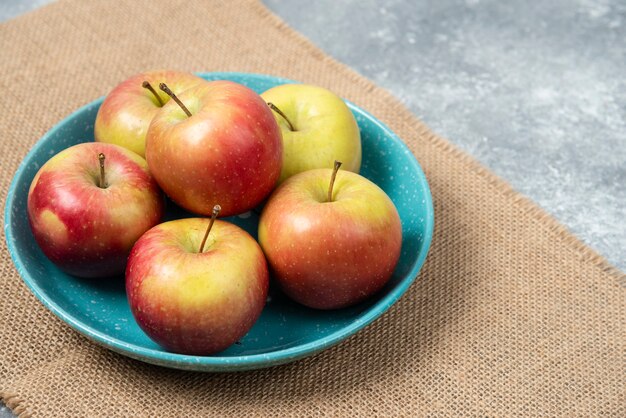 Blue bowl full of fresh apples on marble.