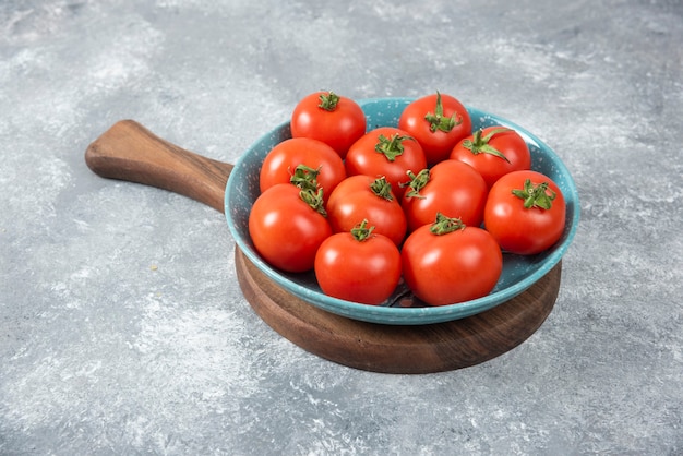 Ciotola blu piena di pomodori freschi rossi su marmo.