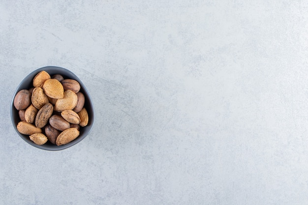Blue bowl full of shelled almonds and walnuts on stone background.