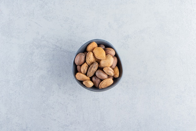 Blue bowl full of shelled almonds and walnuts on stone background.