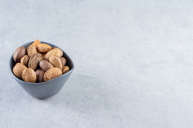 Blue bowl full of shelled almonds and walnuts on stone.