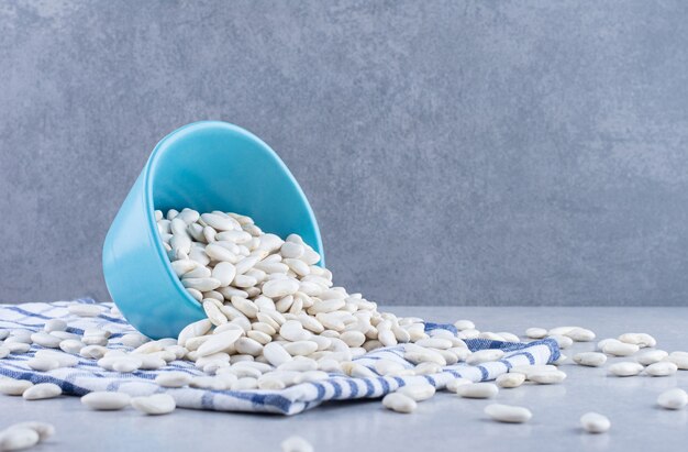 Blue bowl lodged in a scattered heap of navy beans on folded tablecloth on marble surface