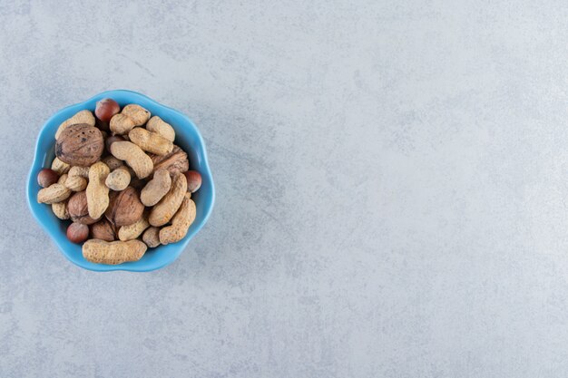 Blue bowl of organic nuts placed on stone background.