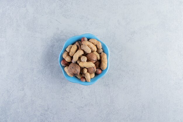 Blue bowl of organic nuts placed on stone background.